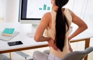 Overworked woman with back pain in office with bad
